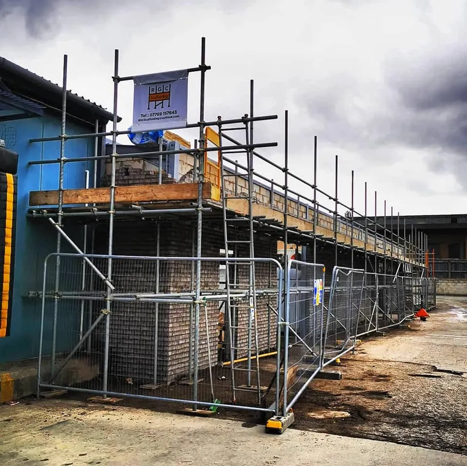 Long run of scaffold with heras fencing along the elevation of an industrial unit