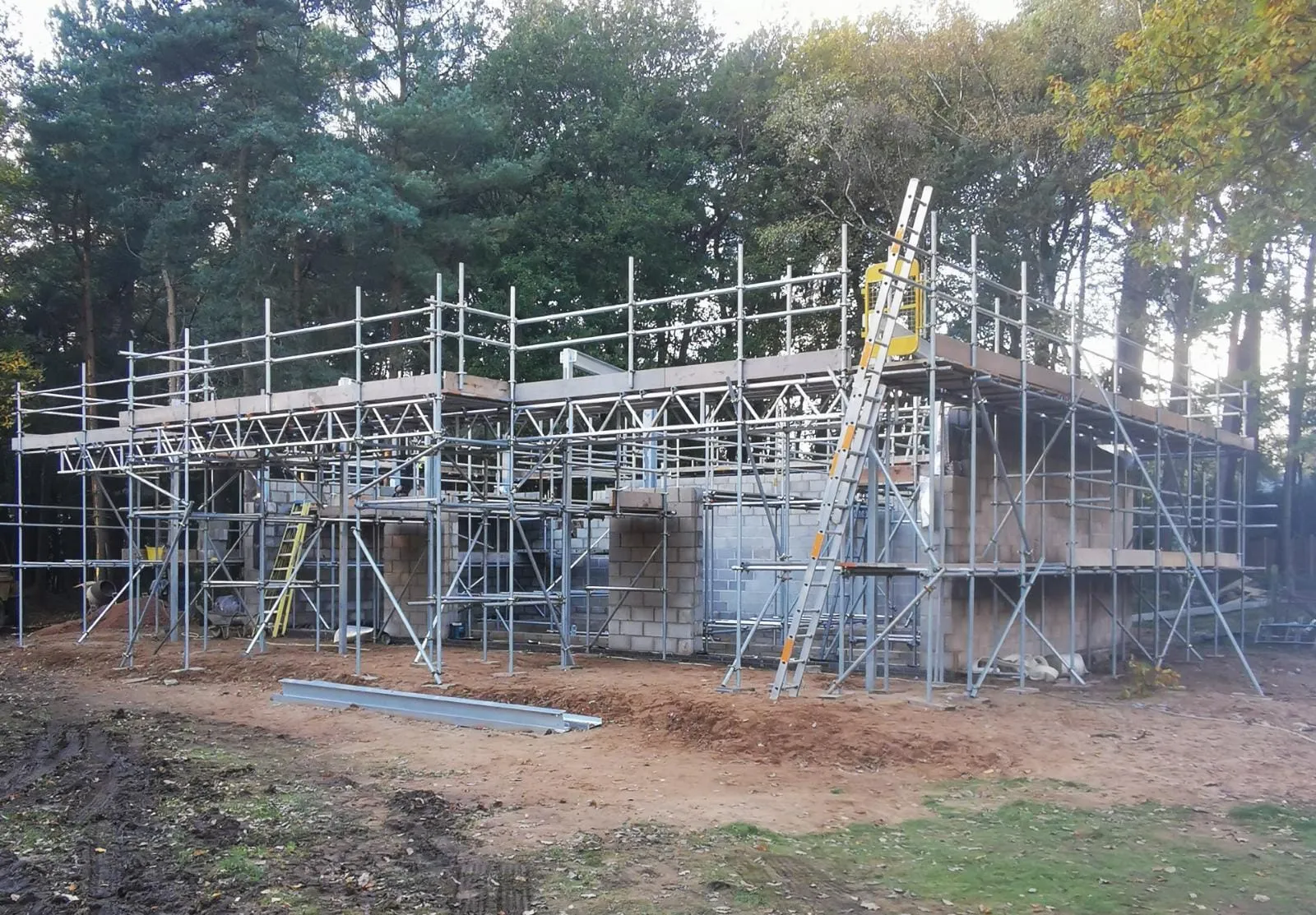 Scaffold erected around a single-storey new build under construction on a woodland plot